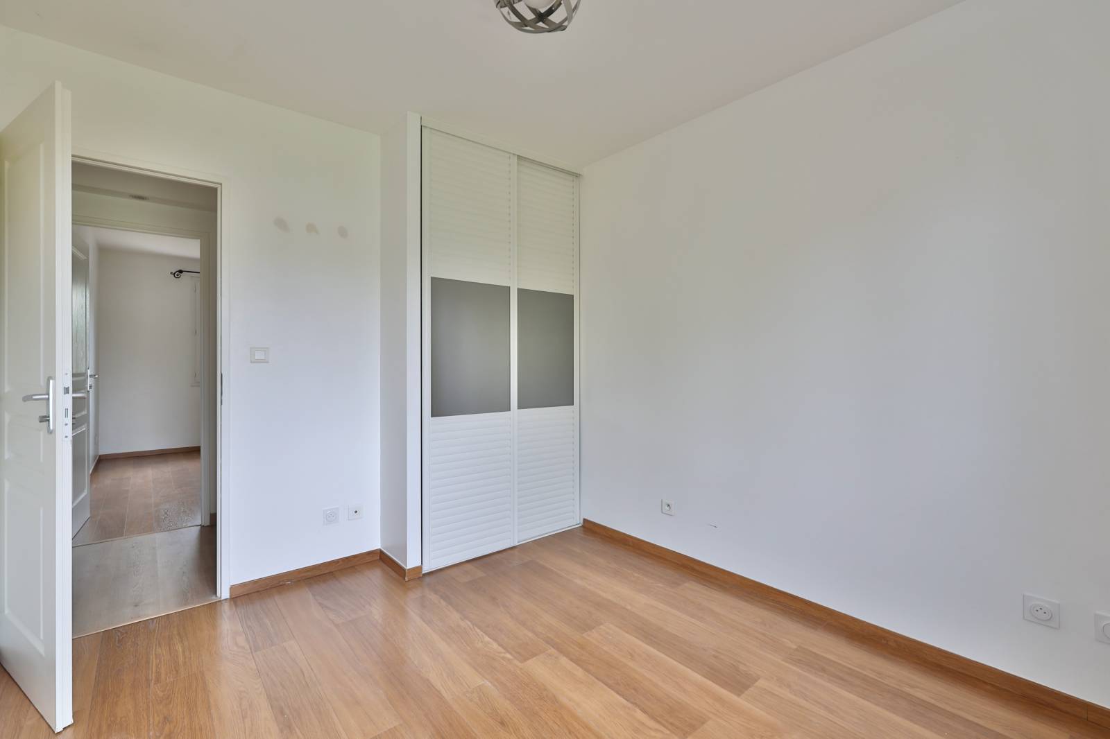 Chambre lumineuse exposée est avec placard mural intégré et parquet bois – espace nuit fonctionnel et confortable dans maison familiale à Vaulx-en-Velin